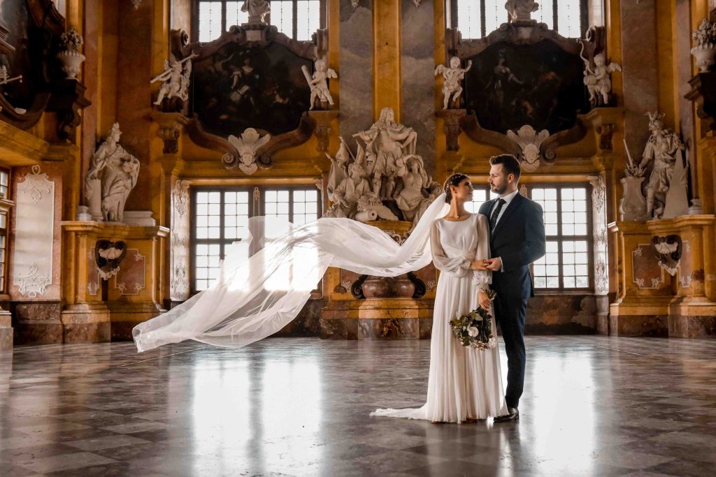 Sesja ślubna pary młodej w pałacu – elegancka fotografia ślubna z rozwianym welonem w zabytkowym wnętrzu