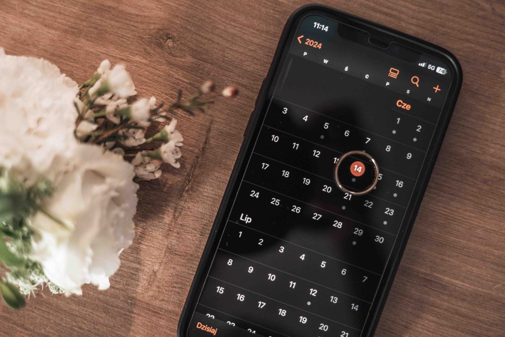 Telefon z kalendarzem i zaznaczoną datą ślubu obok kwiatów – przygotowania do dnia ślubu, detal ślubny