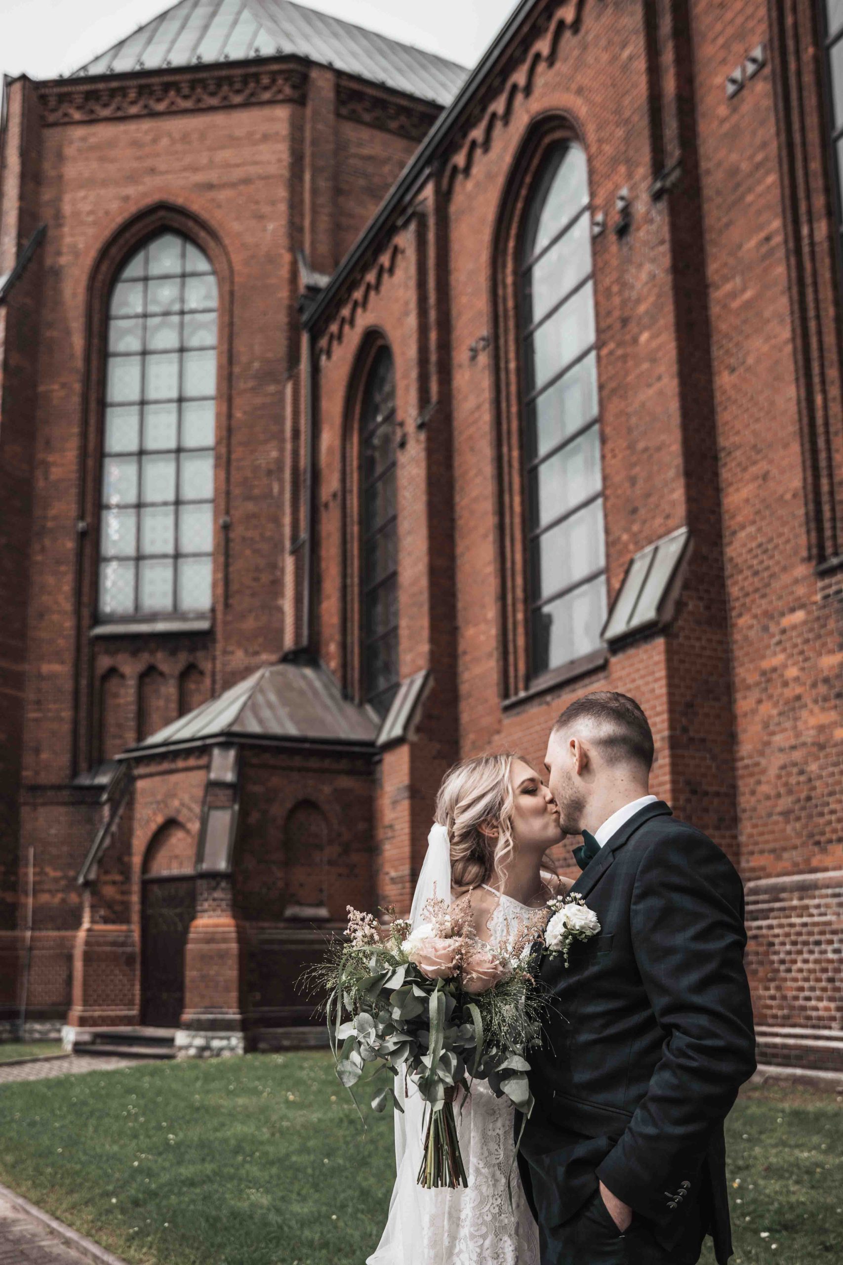 Pocałunek pary młodej przed ceglaną architekturą kościoła w Częstochowie, romantyczne zdjęcia ślubne